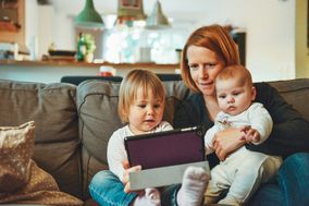 Mother sitting on couch with two children in her lap, looking at ipad together.